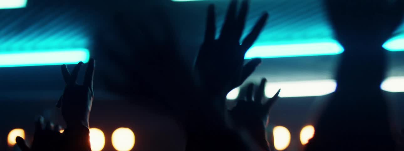 People hands waving in a concert with lights and a person on stage in the background