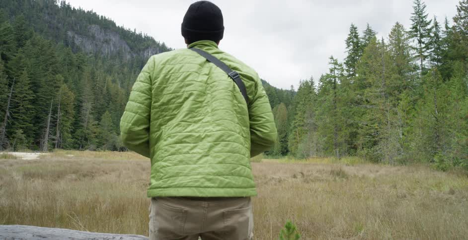 A white man wearing a coat and a hat takes a photograph of a nature scene