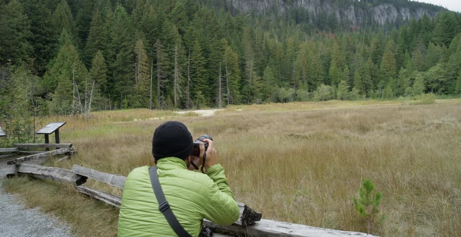 A white man kneels by a wooden fence and takes a nature photograph