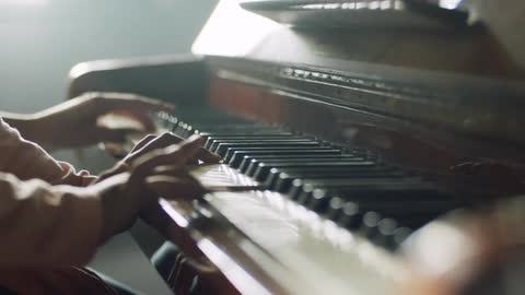 A man and a woman sit at a piano and play together