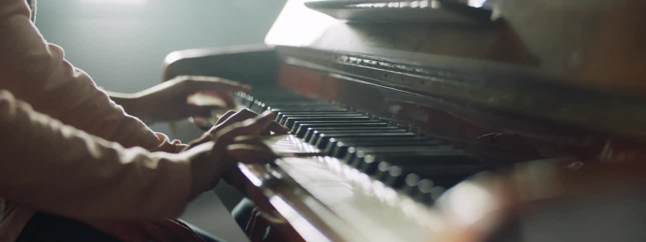 A man and a woman sit at a piano and play together