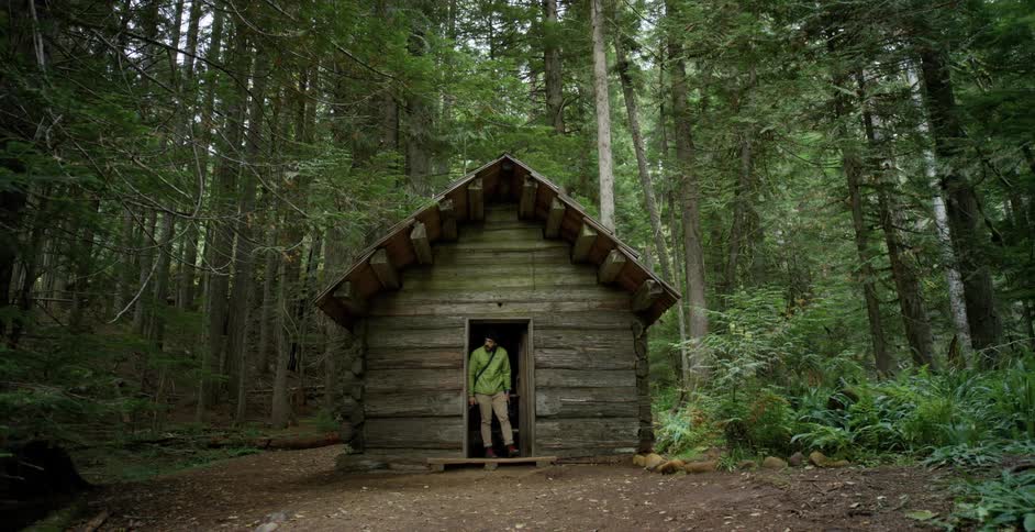 A man walks out of a hut in a forest