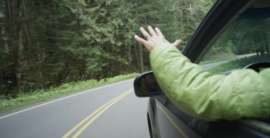 A man moves his arm around through the window of his vehicle while driving