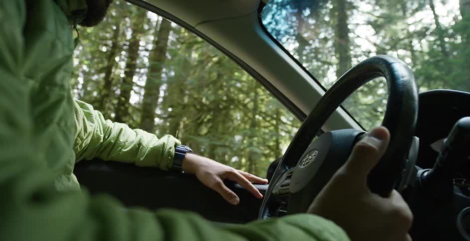 A white man drives a car through a forest