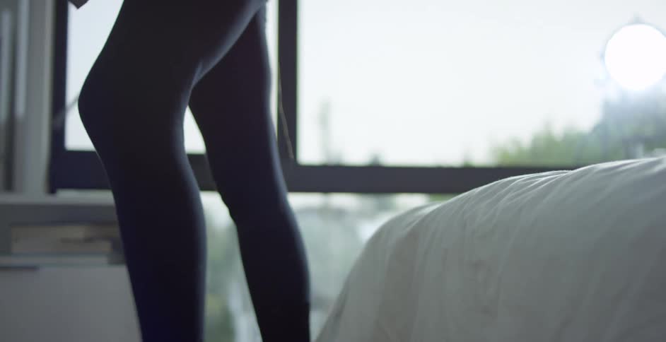 Woman with black tights sitting on a bed packs a blue backpack and stands up to go