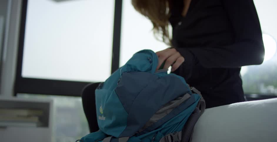A teenager sits on her bed and puts things in her backpack