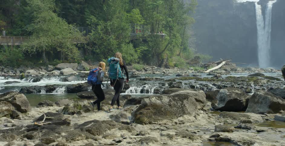 Two girls hiking across rocks towards a waterfall in the canyon