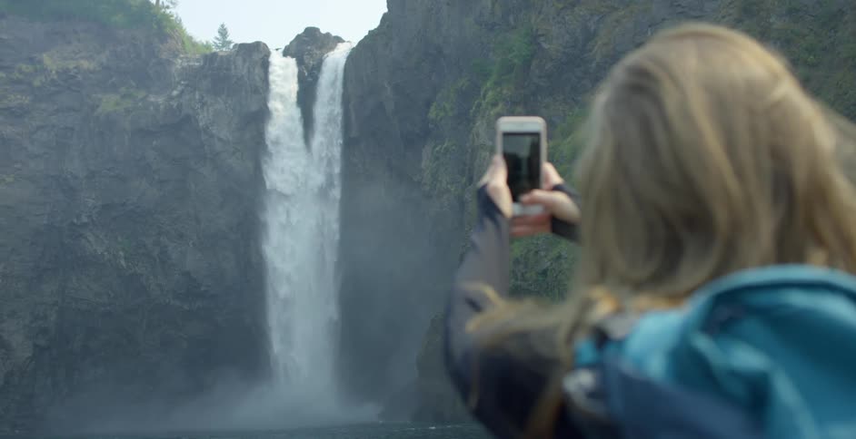 A woman uses a smartphone to take a picture of a natural waterfall