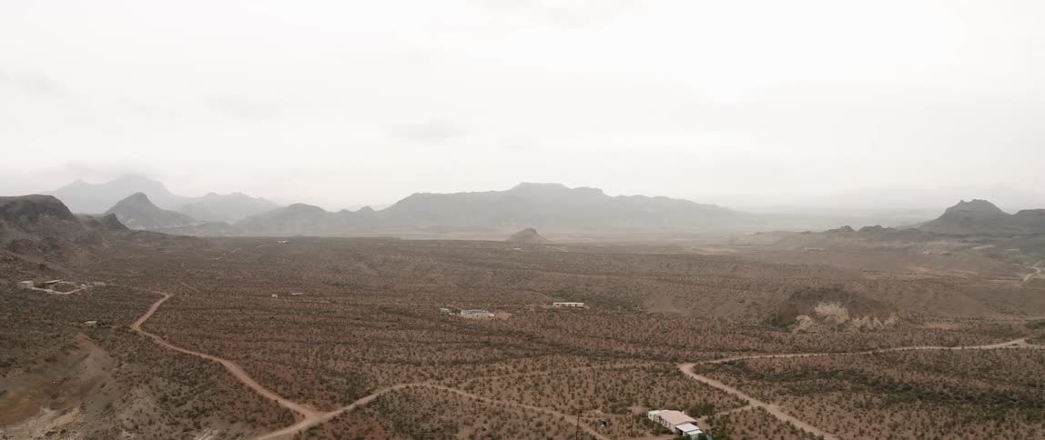 A desert with a house and dirt roads with mountains and the sky in the background