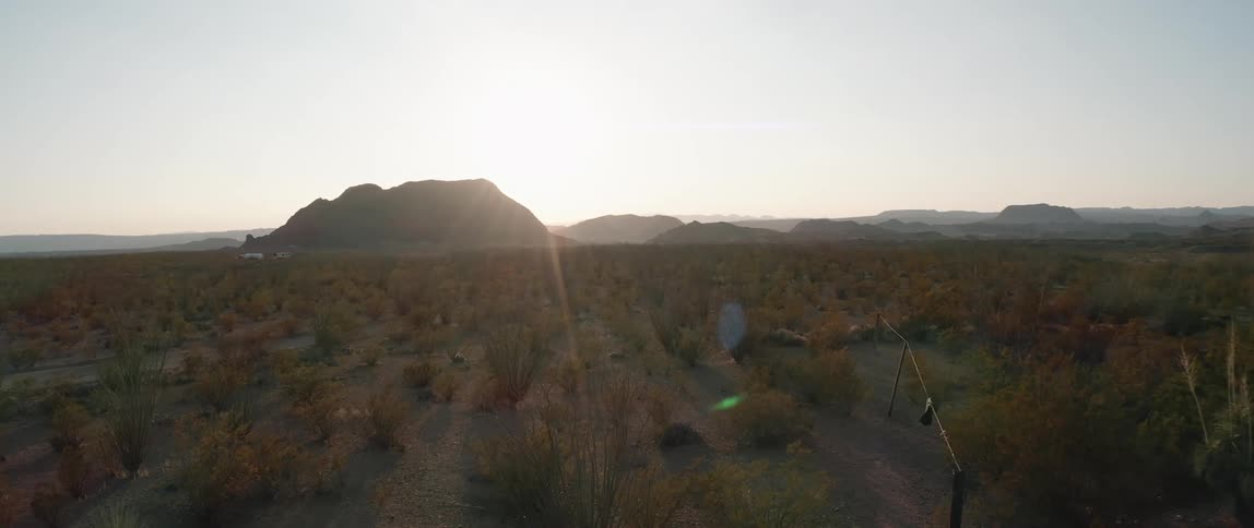 Clothes on clothesline sway in breeze on plain covered in scrub as sun brightens horizon over mountains