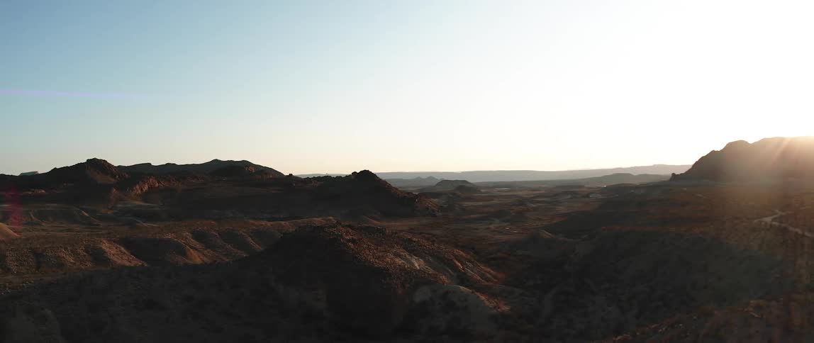 Sun shines on horizon over rough terrain of mountains and valleys