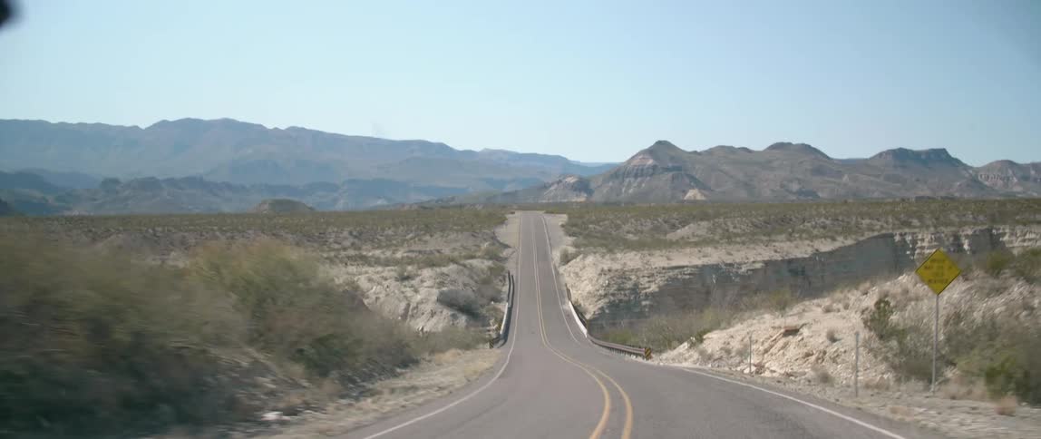 A vehicle travels down a curvy two lane road that leads to a canyon