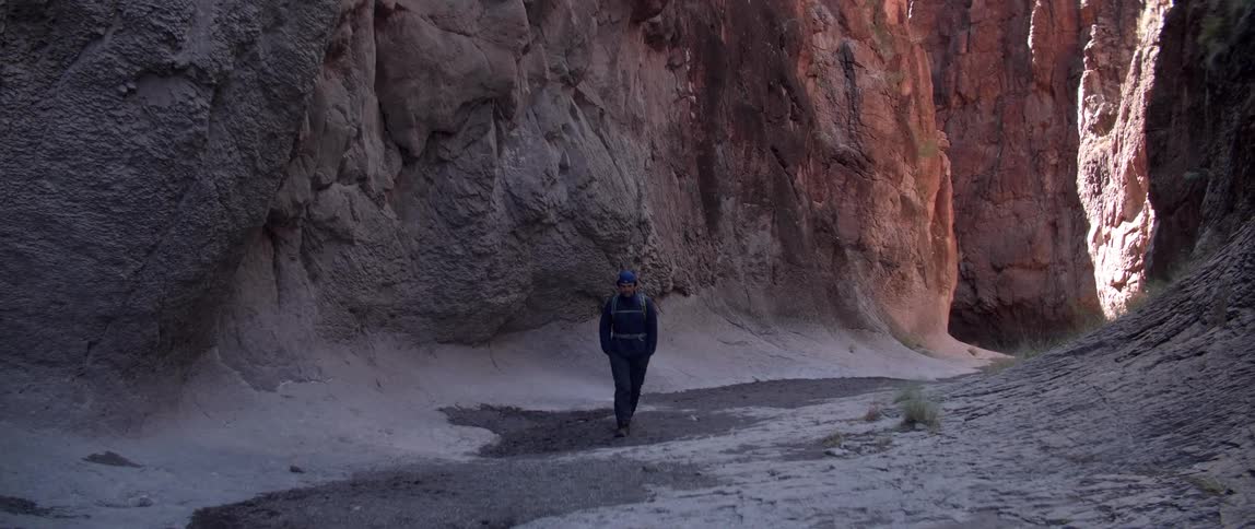 A man hikes at the base of a canyon