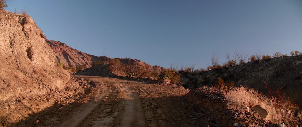 A dirt road with mounds of dirt next to it leading to a canyon