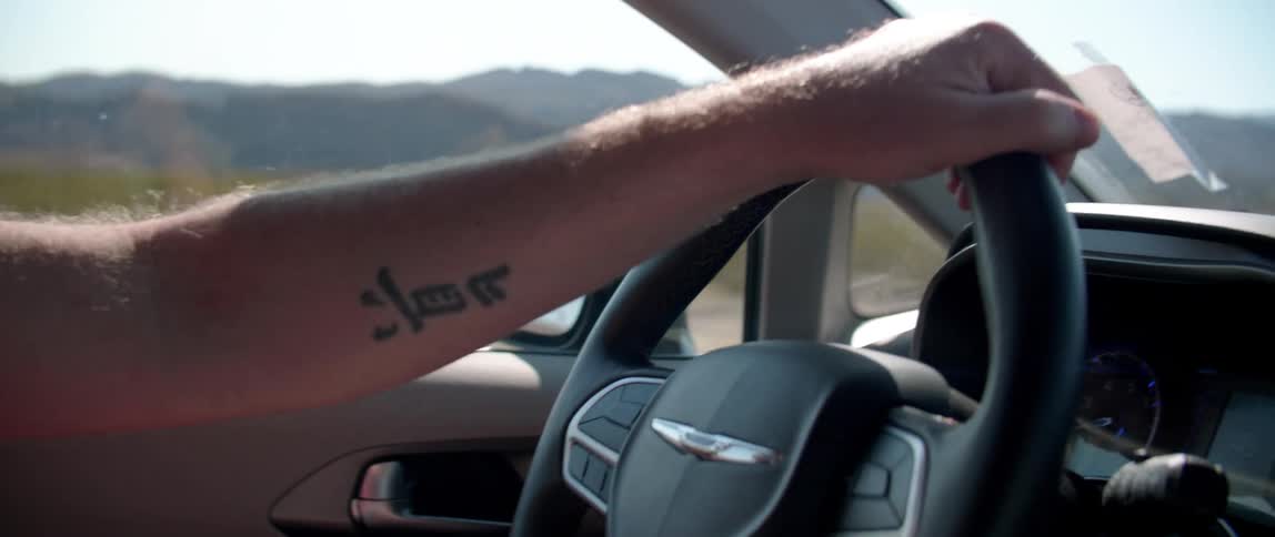 A white man drives a car through a desert area