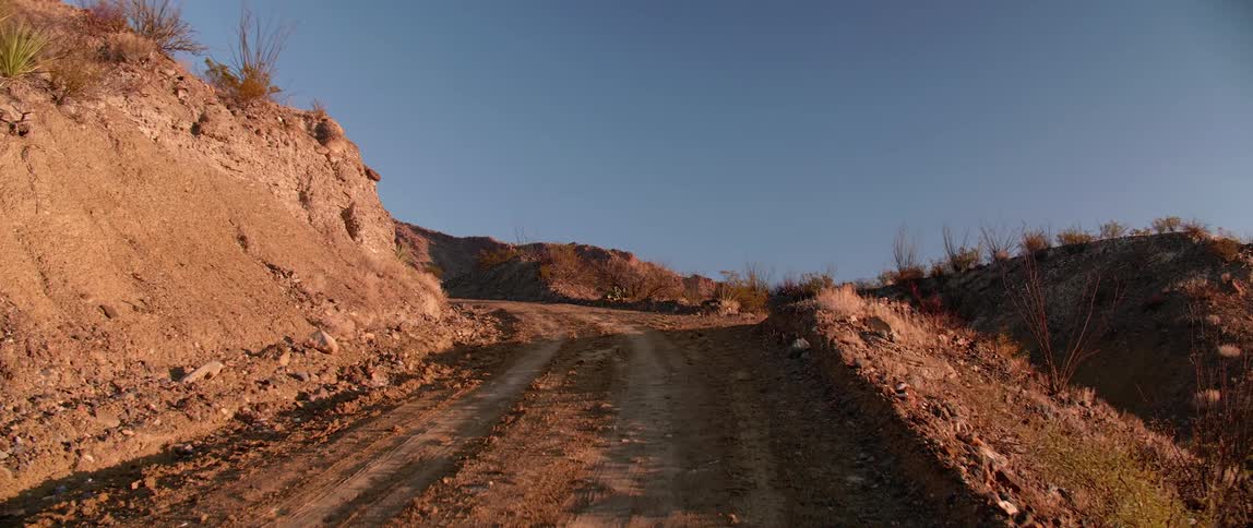 Rural dirt road with tire tracks in the dirt on the hills at sunset