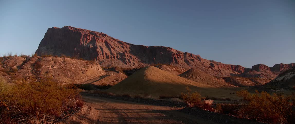 A dirt road runs through a desert terrain near hills and mountains