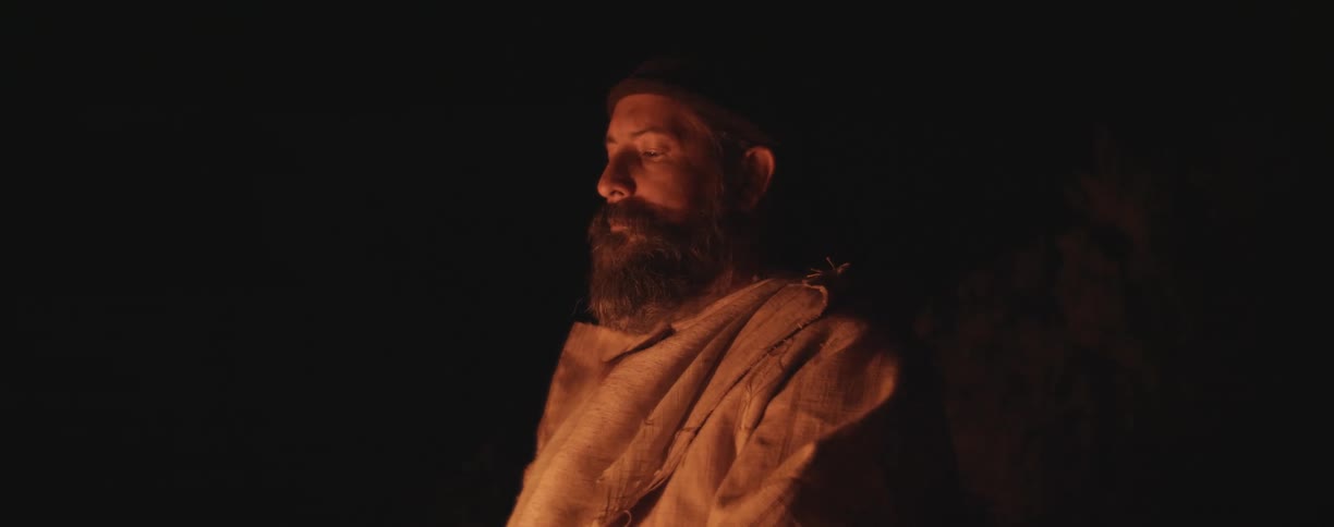 A man looks down at the campfire at night