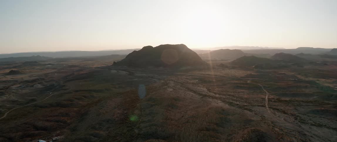 Sun shines on horizon behind mountain in midst of rough terrain an lower mountains