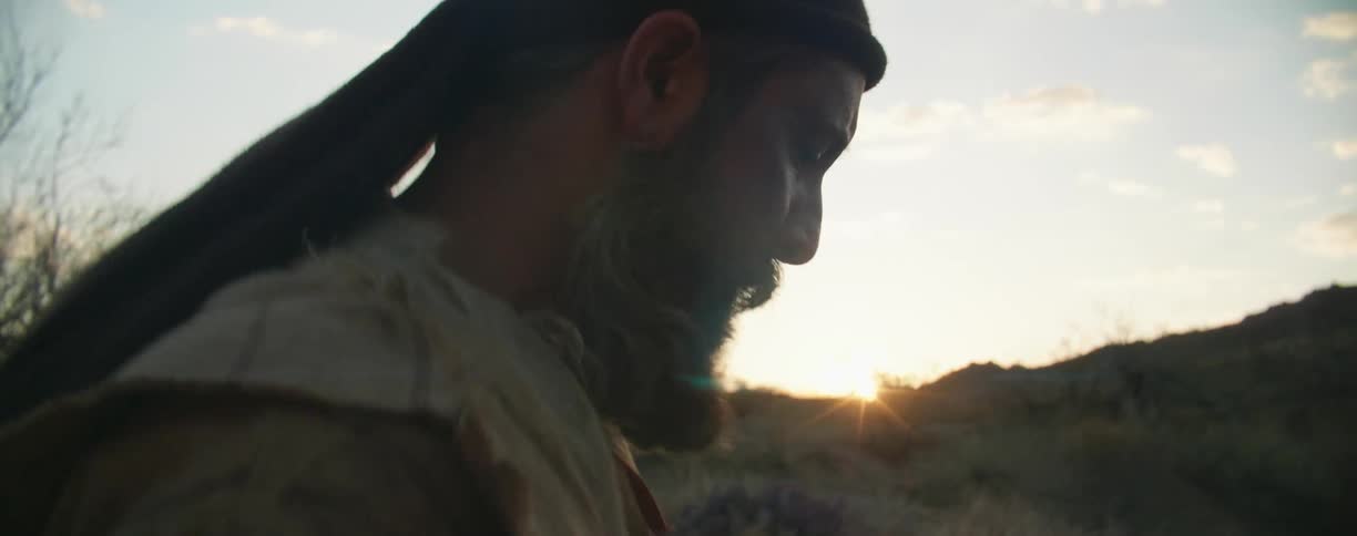 Sun hovers just below horizon as man quickly walks across dimly lit terrain