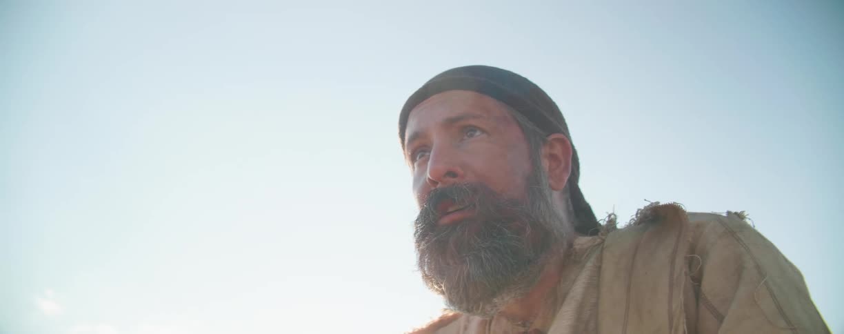 A white man looks down as the sun shines down on him and then looks ahead at the landscape