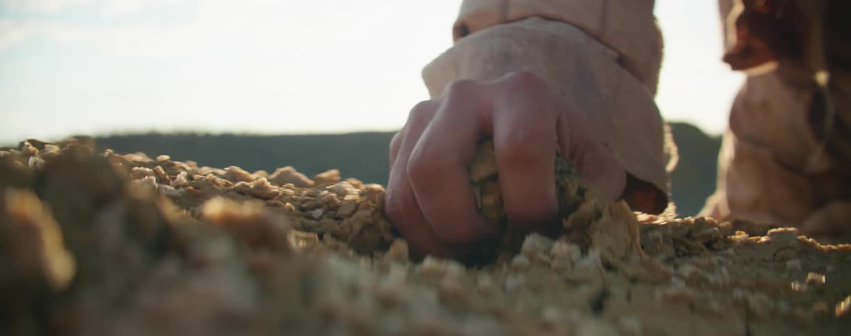 A person grabs a handful of rocks and soil while knelt in the desert