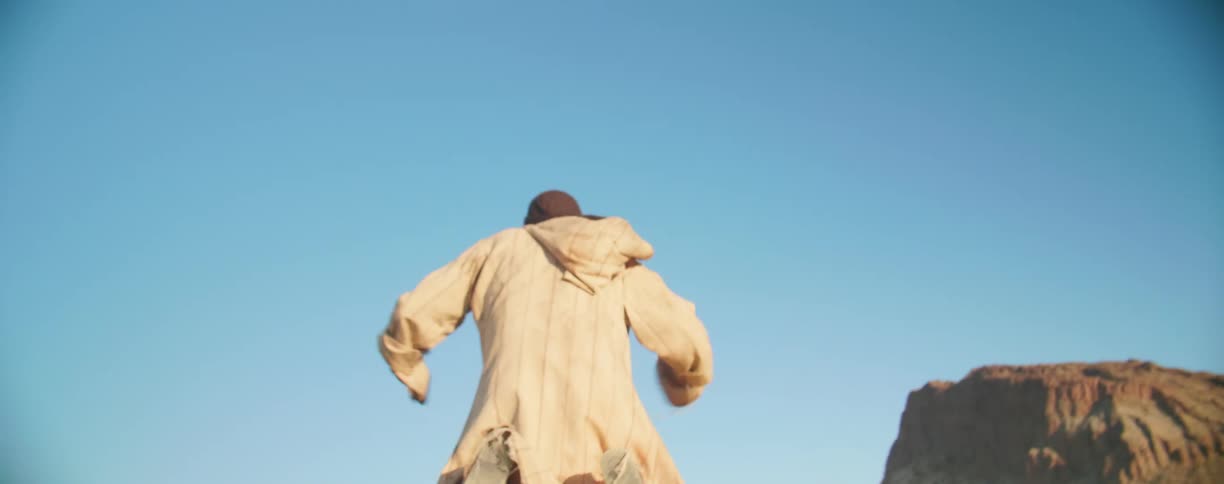 Man wearing a robe runs through the desert and falls on his knees