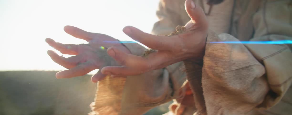 Man fearfully filters dirt and sand through his hands on the desert at sunset
