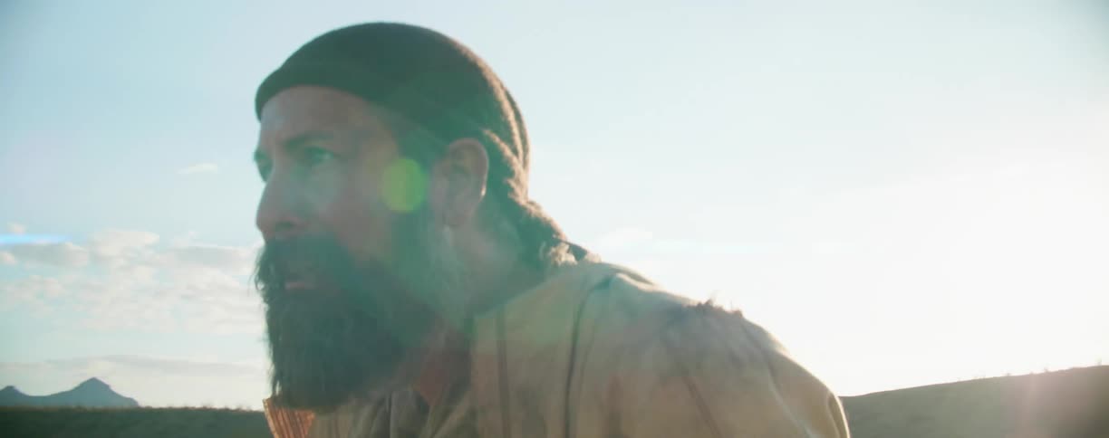 Tired bearded man stands in the desert near hills at sunset