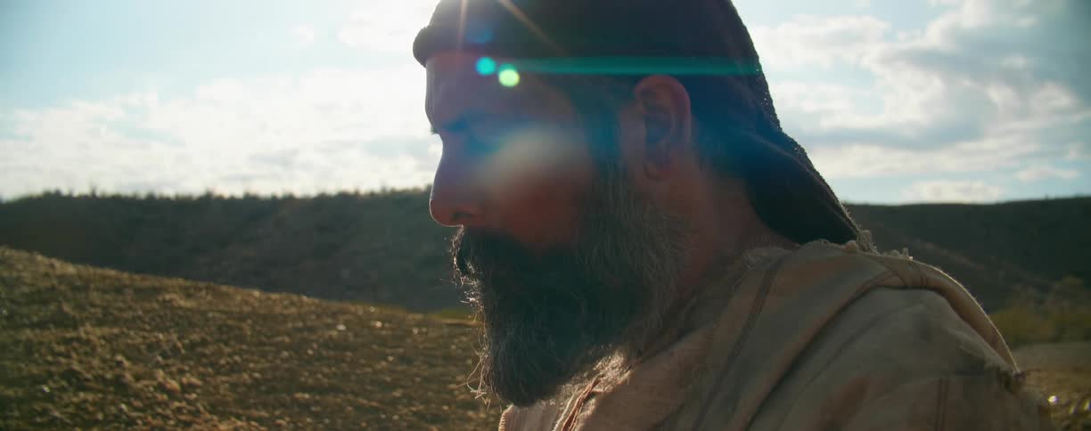 A man in a desert praying with the sky and clouds in the background