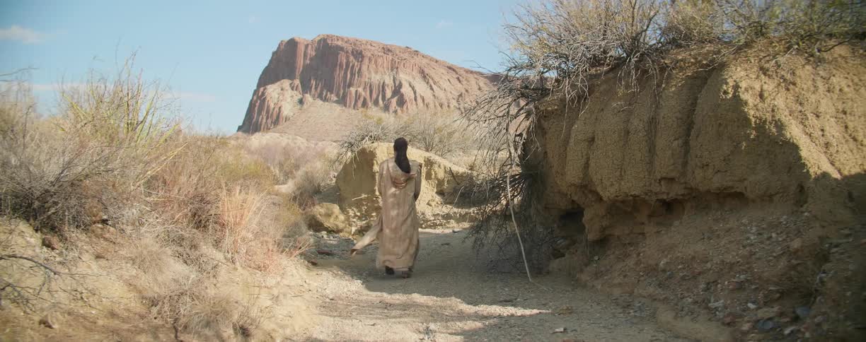 A person walks along a dirt path through an arid wilderness