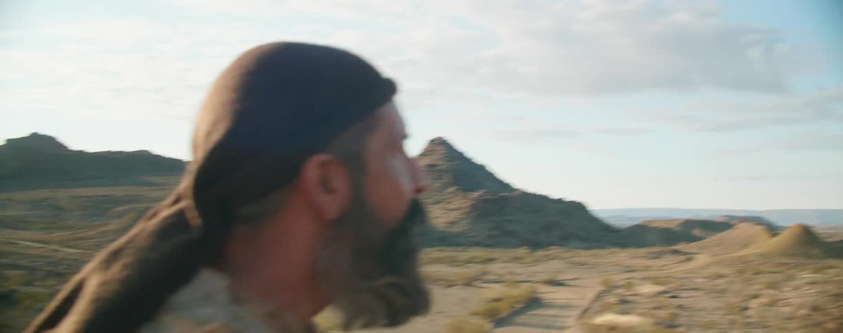 Man wearing robes looks around in the desert at sunrise