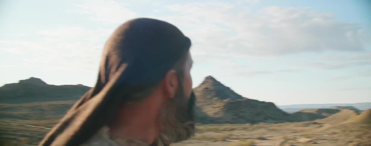 Man stands among rough terrain looking over hills and mountains