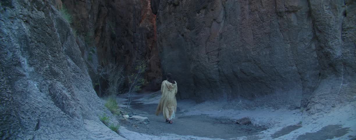 A person with a coat walking in the bottom of a canyon