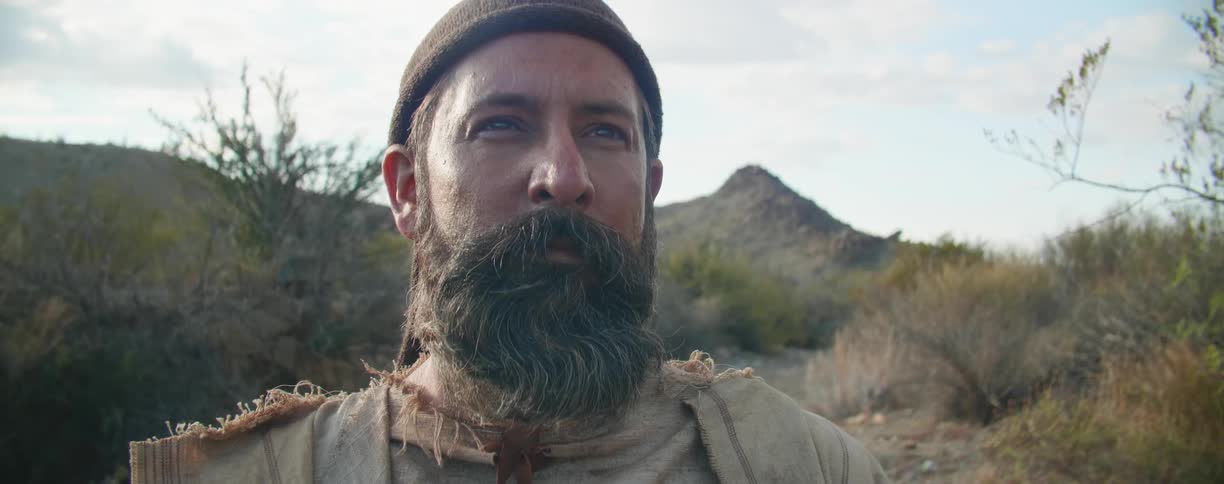 A white man with a beard stands in a desert