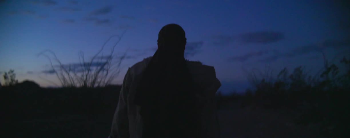 A man is walking in the dark field at sunset