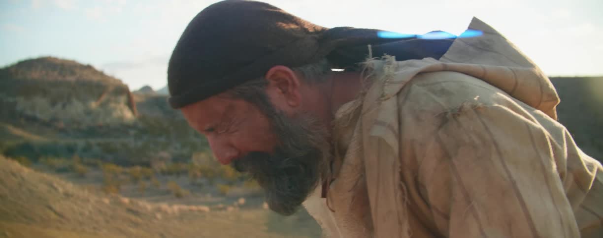 Bearded man yells as he stands in a field under a sunny sky