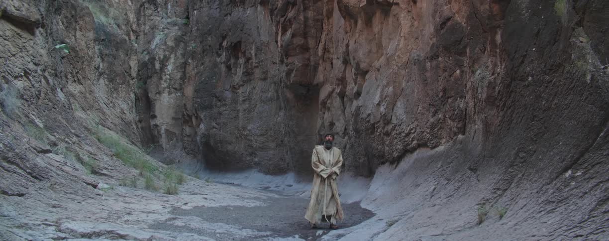A man with a brown robe walking in the bottom of a canyon