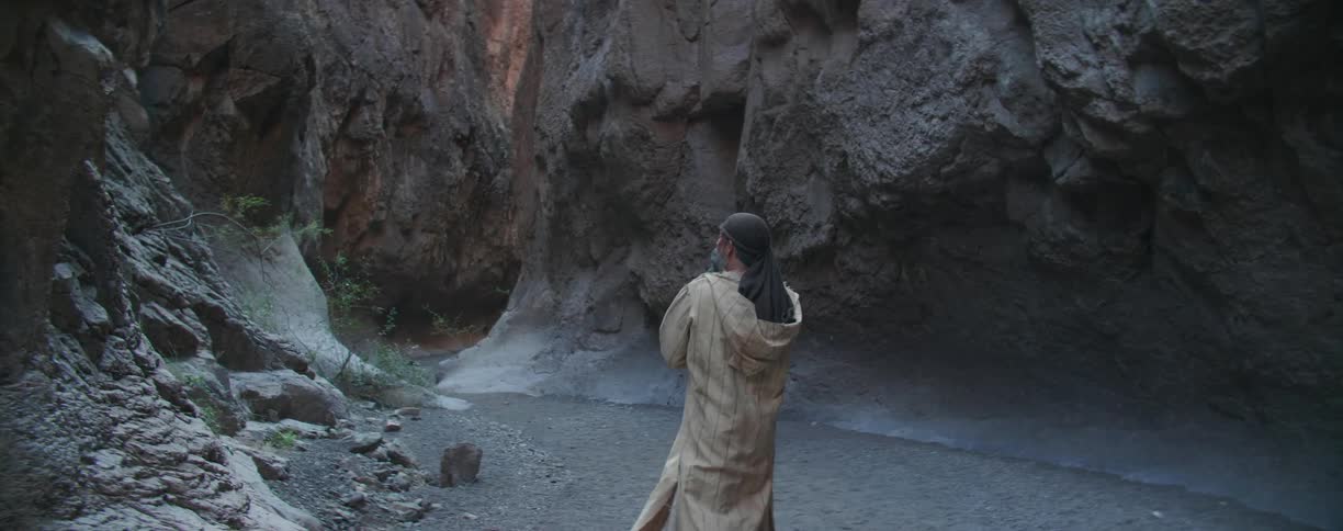 Man wearing robe and cloth head covering walks into ravine