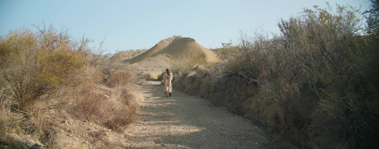 A man walking on a dirt road with a hill and the sky in the background