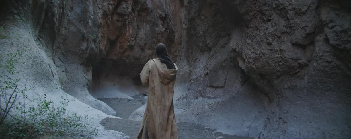 A man with a coat walking in the bottom of a canyon