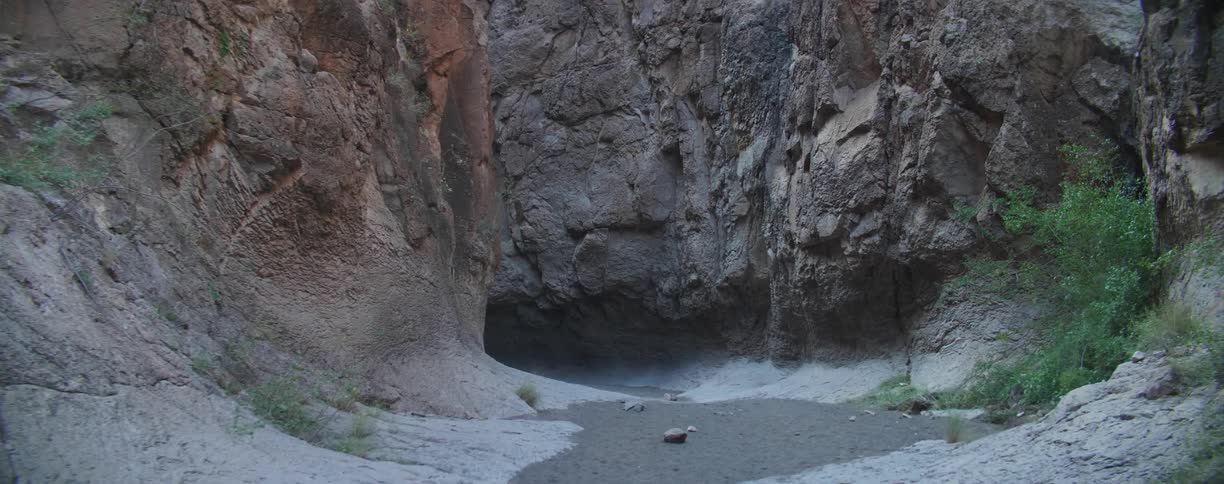 A dirt path leading to a cave at the bottom of a canyon