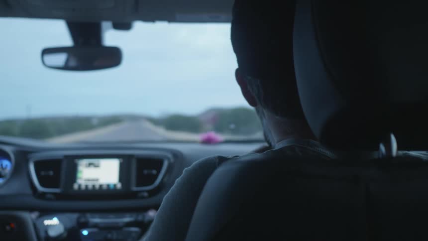 Man sitting on the copilot seat of a car talks to the pilot while driving on a rural road