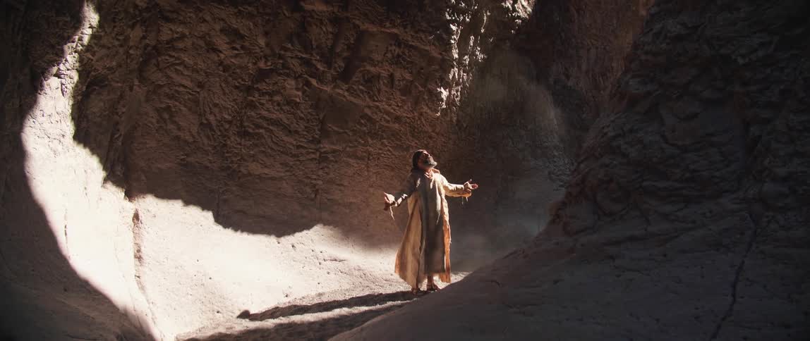 A man stands at the base of a canyon with his arms extended as he prays