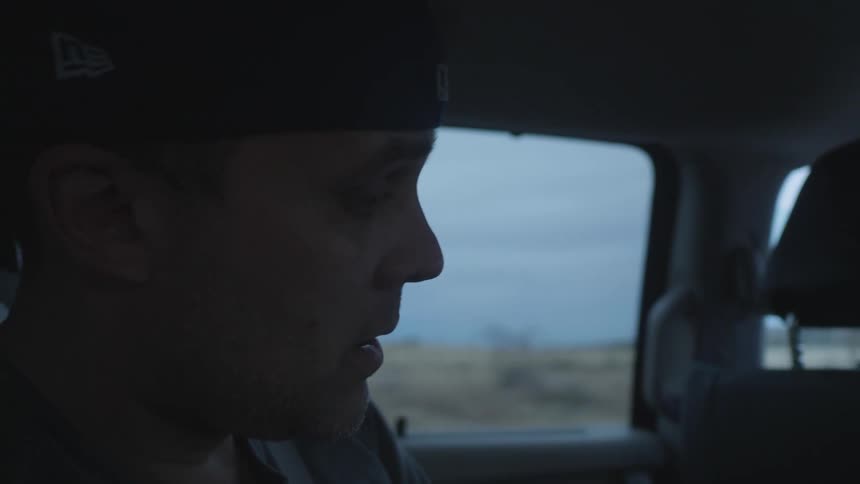 Male wearing a seat belt sitting in back seat of a moving vehicle nods his head slightly to a beat