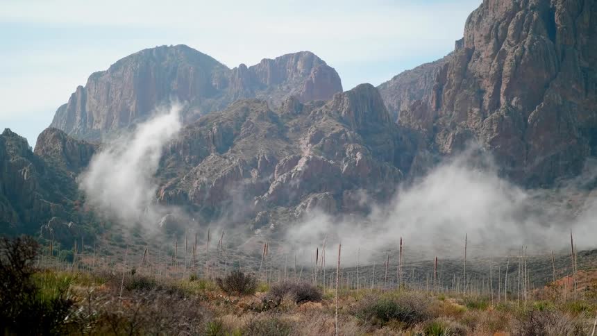 Smoke floats and rise up over a valley toward rocky ridges