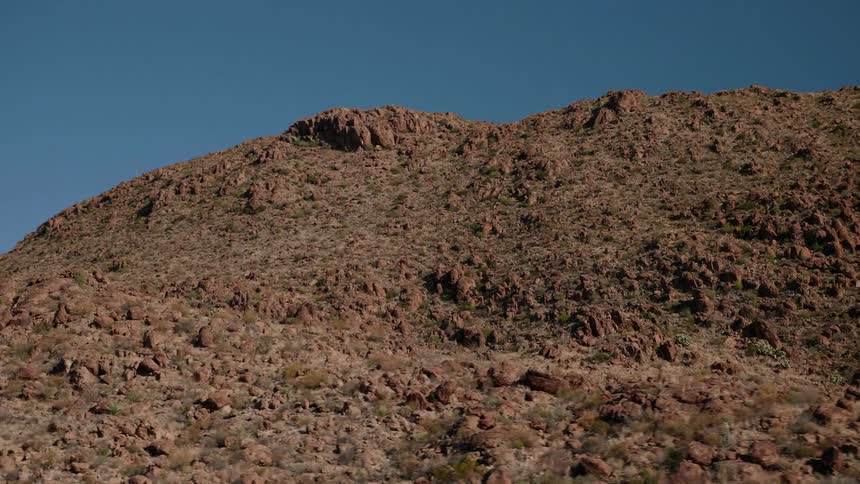 Rough lightly vegetated mountain sides and slopes stretch under azure blue sky