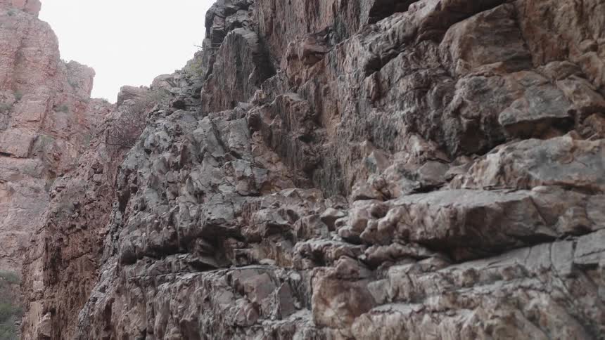 A rocky cliff with the sky and clouds up above