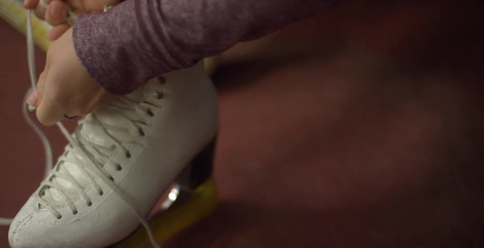 A woman laces up her white ice skates