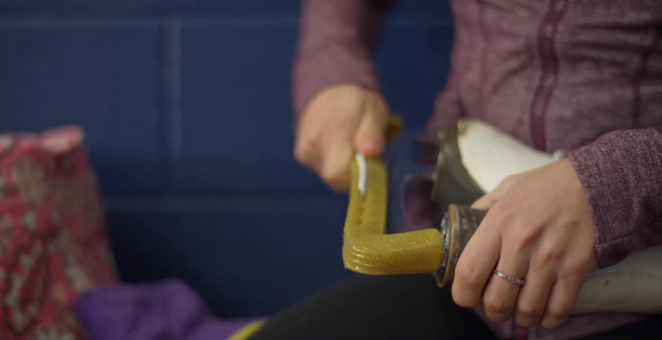 An ice skater sits on a bench as she covers the blade of her skates